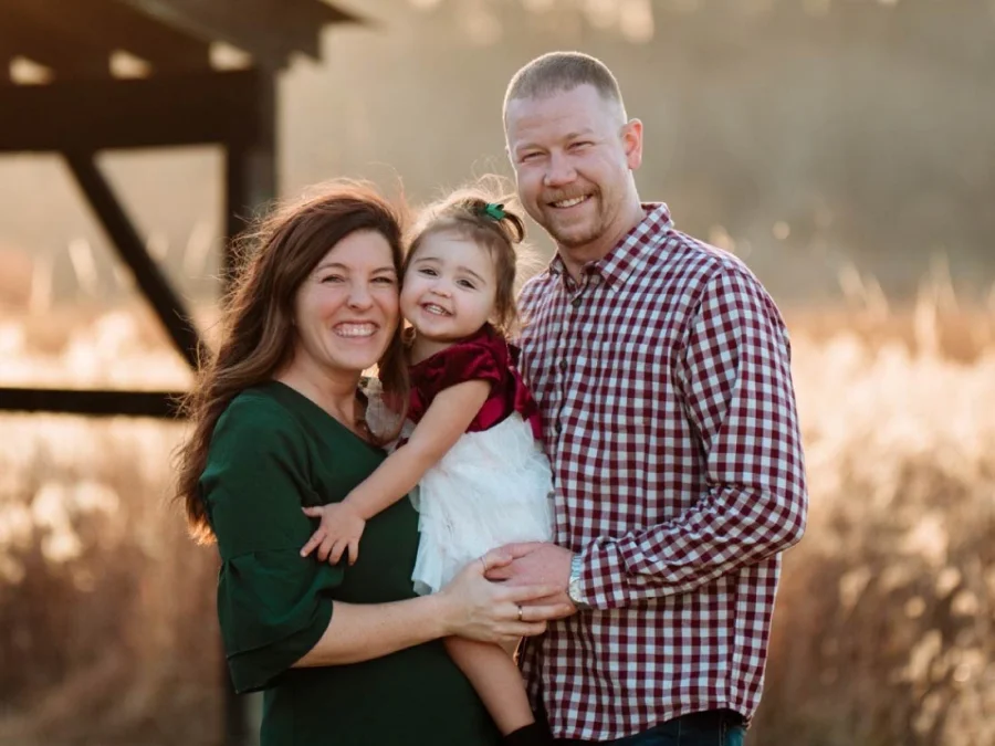 A mother and father holding their young daughter outdoors at golden hour
