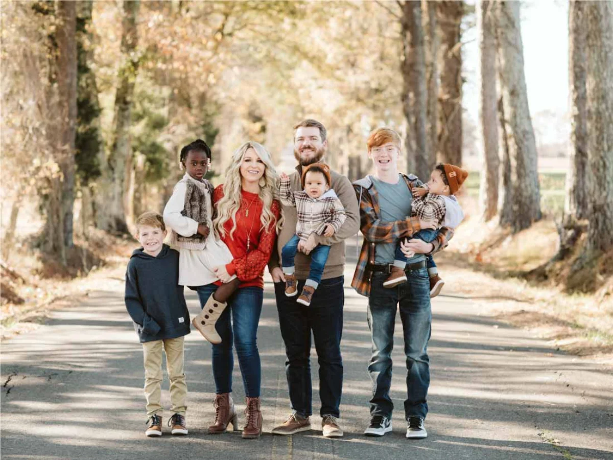 A family of seven standing together on a tree-lined road in autumn